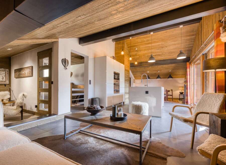 Experience the warmth of this stunning chalet, featuring a cozy living area with a rustic wooden ceiling and a modern kitchen.