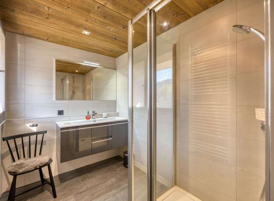 This modern bathroom features a sleek, gray vanity with ample storage and a stylish black chair with a fur seat.
