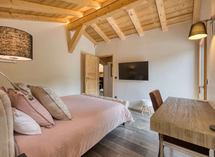 This cozy bedroom features a wooden ceiling and a comfortable bed with soft pink bedding.