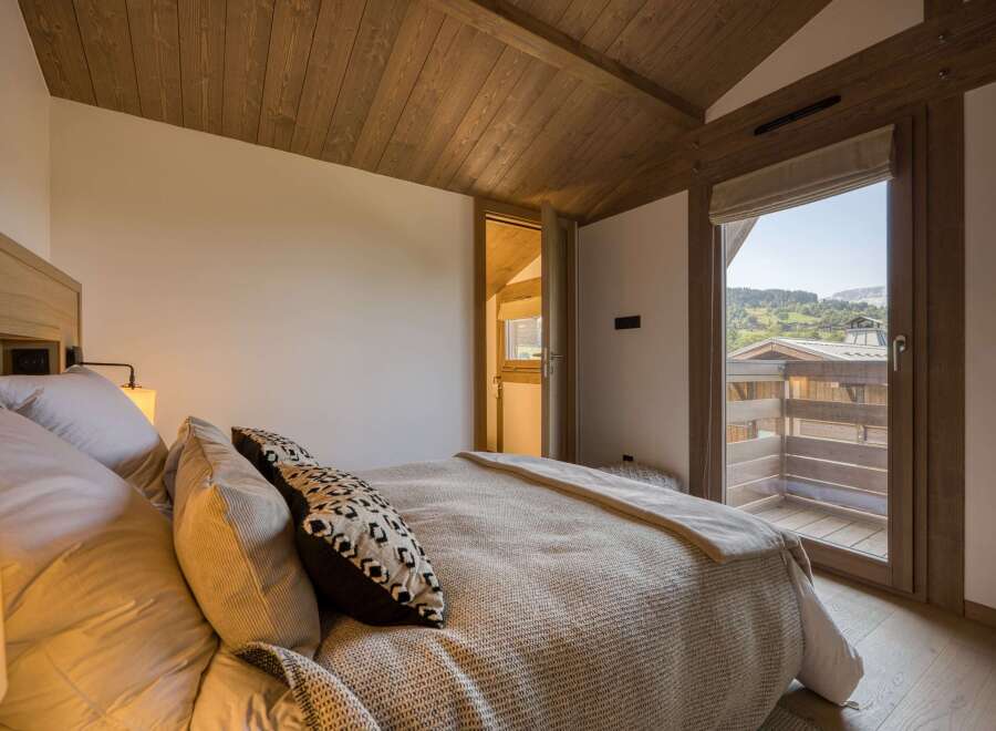 This cozy bedroom features a wooden ceiling and a large window offering stunning views of the surrounding landscape.
