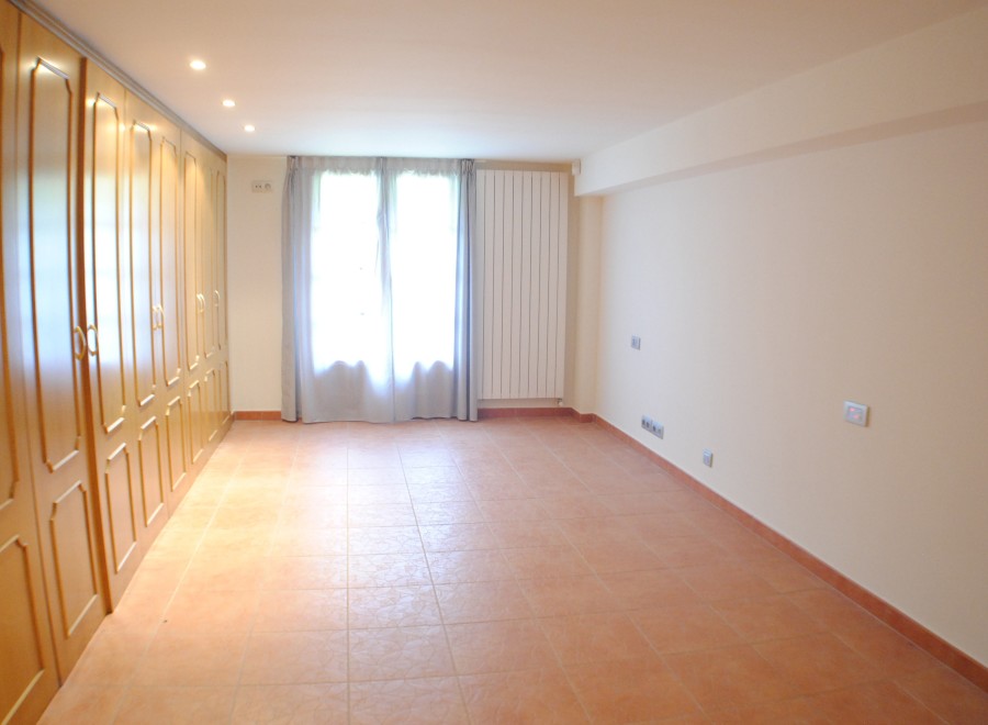 Spacious room with terracotta tile flooring and built-in wooden wardrobes.