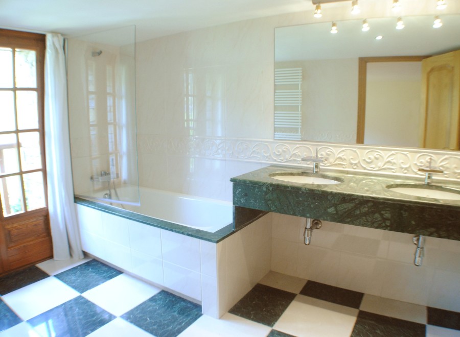 This luxurious bathroom boasts a spacious bathtub with a glass enclosure, complemented by a stylish green marble double vanity with modern fixtures.