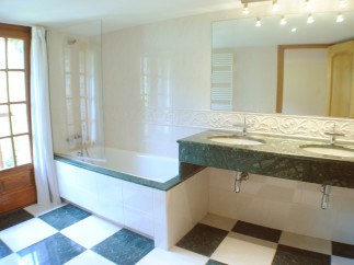 This luxurious bathroom boasts a spacious bathtub with a glass enclosure, complemented by a stylish green marble double vanity with modern fixtures.