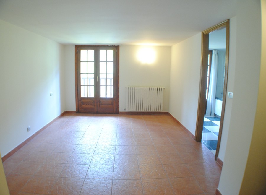 This spacious room boasts terracotta tile flooring and large wooden doors that lead to outdoor access.