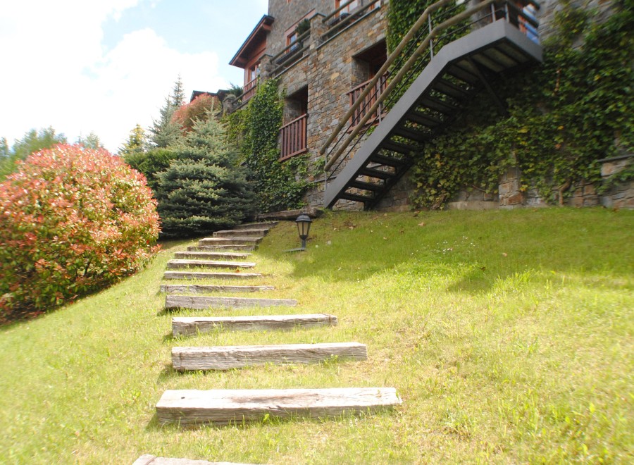 This stunning property boasts a charming stone exterior, lush landscaping, and a unique wooden staircase leading to a modern metal staircase.