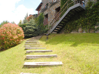 This stunning property boasts a charming stone exterior, lush landscaping, and a unique wooden staircase leading to a modern metal staircase.