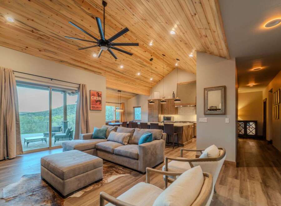 This stunning property boasts a spacious living area with a vaulted, wood-paneled ceiling and a modern ceiling fan.