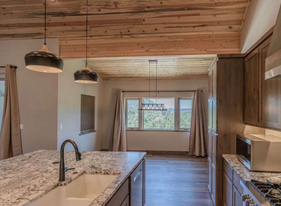 Experience breathtaking mountain views from this stunning kitchen, featuring a large granite island with a farmhouse sink and a sleek faucet.