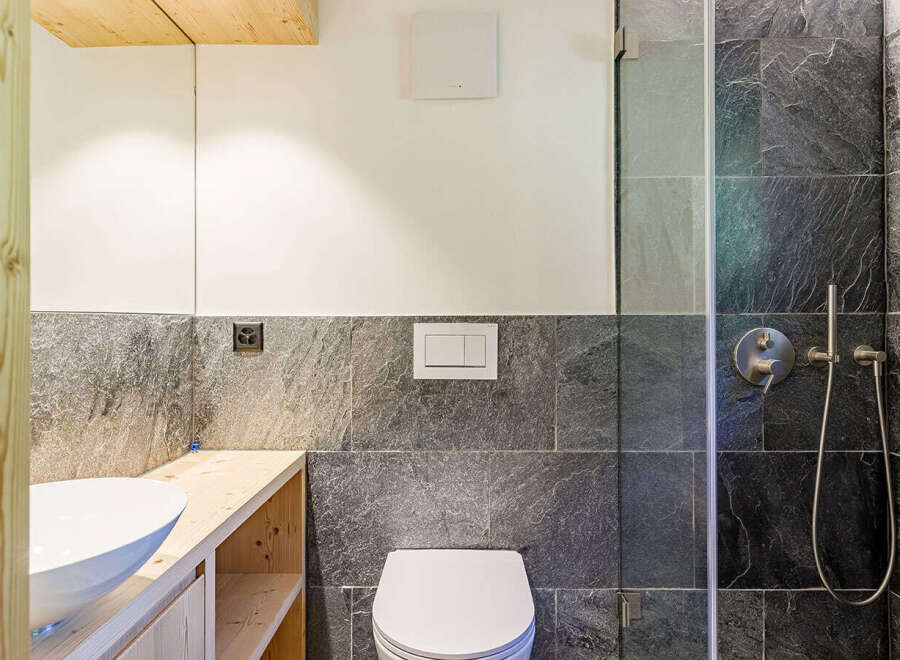 This modern bathroom features a sleek design with dark stone tiles and a wooden vanity.