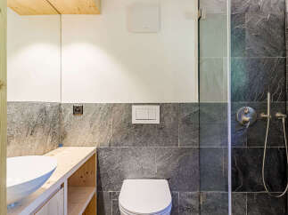 This modern bathroom features a sleek design with dark stone tiles and a wooden vanity.