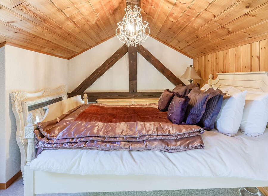 This charming bedroom boasts a cozy and inviting atmosphere with its wooden ceiling and elegant chandelier.