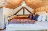 This charming bedroom boasts a cozy and inviting atmosphere with its wooden ceiling and elegant chandelier.