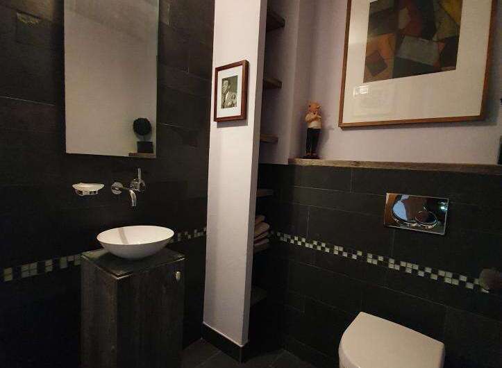 This modern bathroom boasts a sleek design with dark tile walls and flooring, creating a sophisticated ambiance.