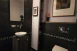 This modern bathroom boasts a sleek design with dark tile walls and flooring, creating a sophisticated ambiance.