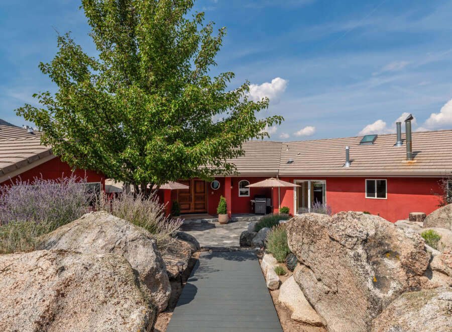 This stunning property boasts a vibrant red exterior, complemented by a lush green tree and natural rock formations.