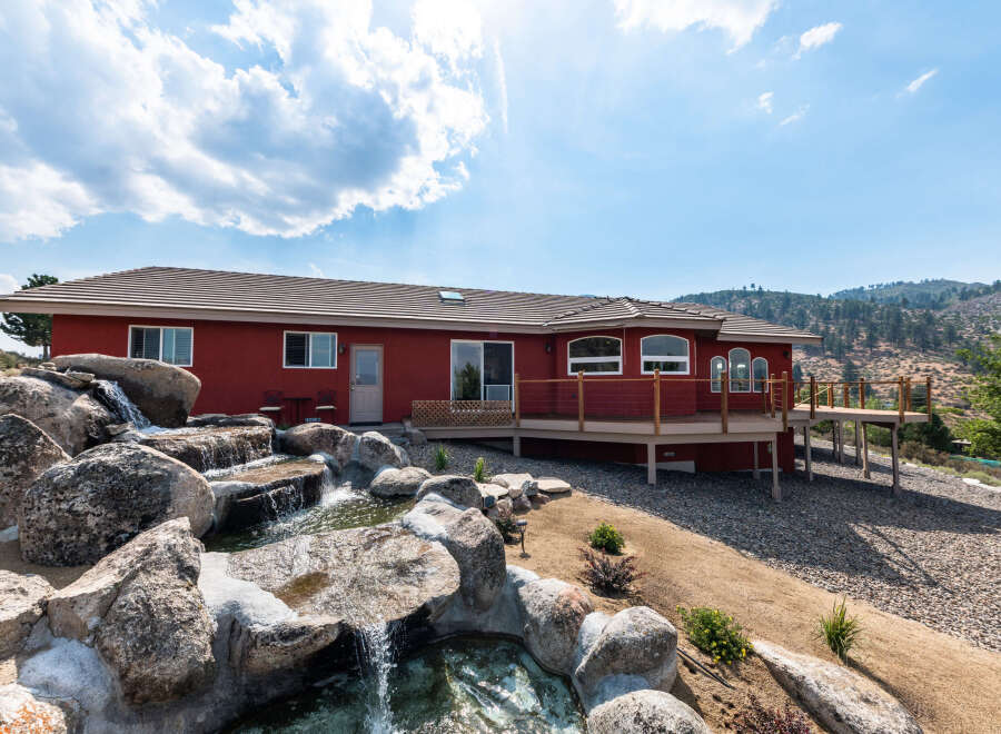 Discover a stunning red-hued home nestled in a picturesque landscape, complete with a cascading waterfall feature.