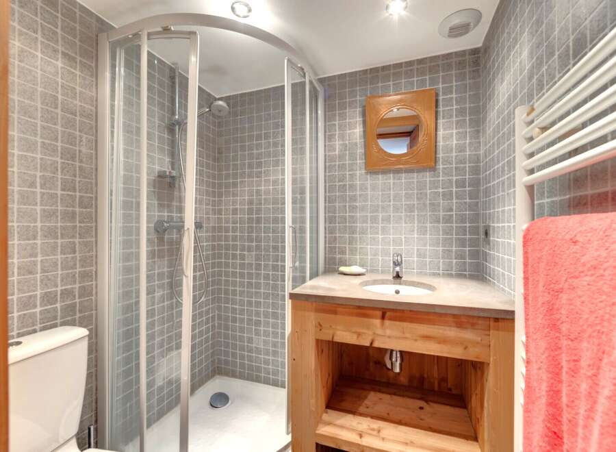 This charming bathroom features a modern shower, a stylish wooden vanity, and a sleek sink.