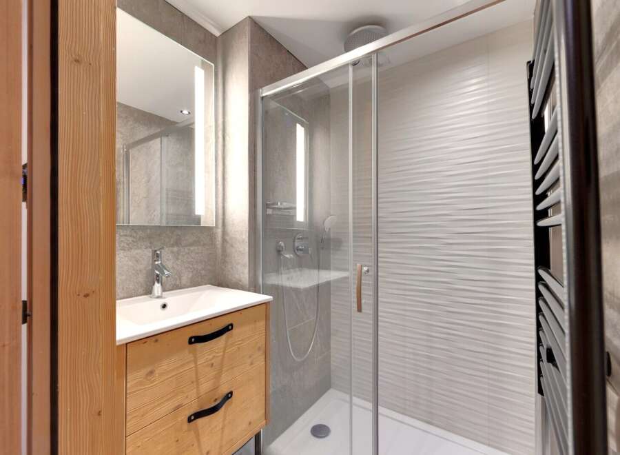 This modern bathroom features a sleek glass shower, a stylish wooden vanity, and a contemporary mirror with integrated lighting.