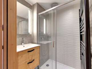 This modern bathroom features a sleek glass shower, a stylish wooden vanity, and a contemporary mirror with integrated lighting.