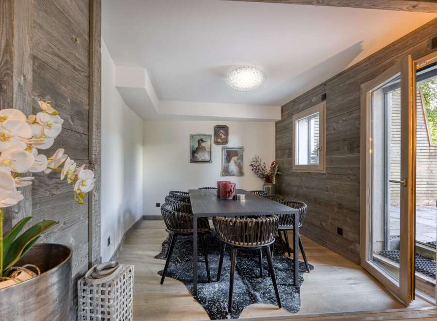This dining room exudes rustic charm with its wood-paneled walls and a striking black dining table.