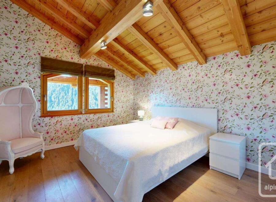 This charming bedroom features a cozy ambiance with its wooden ceiling and floral wallpaper.