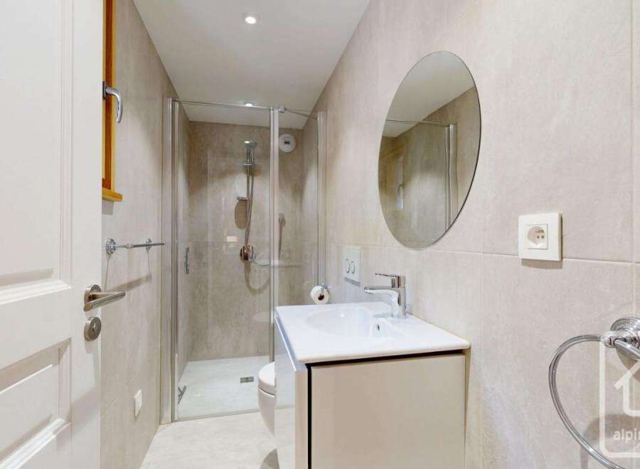 This modern bathroom features a sleek design with a glass shower enclosure, a stylish vanity, and a round mirror.