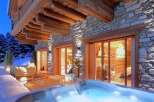 Experience luxury living in this stunning mountain chalet, featuring a private hot tub and a cozy outdoor seating area.