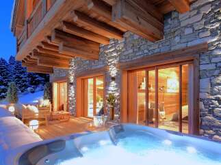 Experience luxury living in this stunning mountain chalet, featuring a private hot tub and a cozy outdoor seating area.