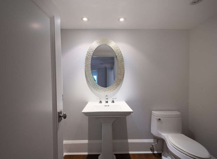 This elegant powder room features a stylish pedestal sink, a decorative oval mirror, and a modern toilet.