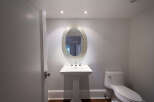 This elegant powder room features a stylish pedestal sink, a decorative oval mirror, and a modern toilet.