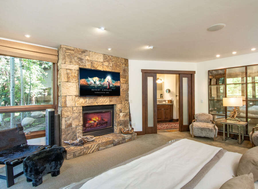 Experience luxury and comfort in this stunning bedroom featuring a cozy fireplace and a large flat-screen TV.