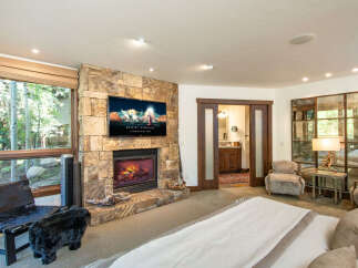 Experience luxury and comfort in this stunning bedroom featuring a cozy fireplace and a large flat-screen TV.