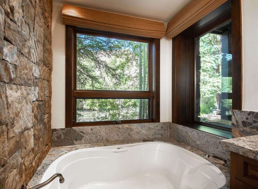 This luxurious bathroom features a stunning stone wall and a large window offering breathtaking views of the surrounding nature.