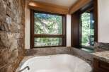 This luxurious bathroom features a stunning stone wall and a large window offering breathtaking views of the surrounding nature.