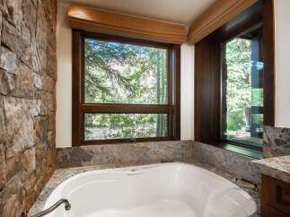 This luxurious bathroom features a stunning stone wall and a large window offering breathtaking views of the surrounding nature.