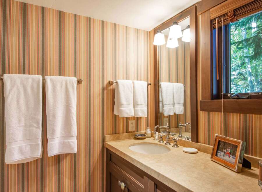 This charming bathroom features a warm and inviting atmosphere with its striped wallpaper and wooden accents.