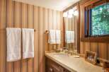 This charming bathroom features a warm and inviting atmosphere with its striped wallpaper and wooden accents.
