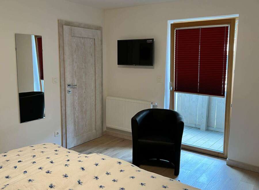 Discover a cozy bedroom featuring a stylish black armchair, a mounted TV, and a full-length mirror.