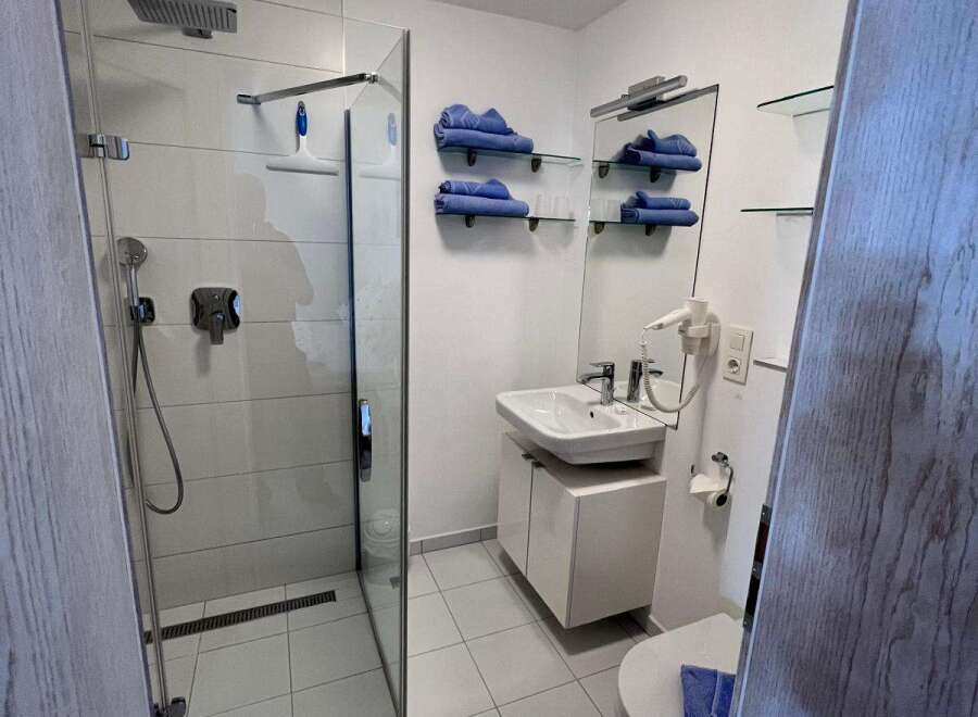 Step into this modern bathroom, featuring a sleek glass shower enclosure and pristine white tiling.