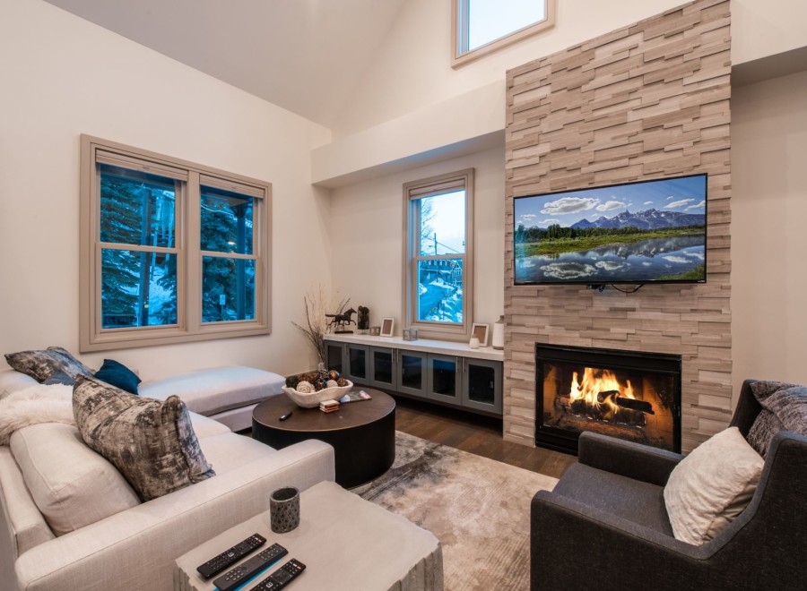 Cozy up by the fireplace in this stunning living room, featuring a large sectional sofa and a wall-mounted TV showcasing breathtaking mountain views.