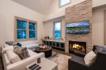 Cozy up by the fireplace in this stunning living room, featuring a large sectional sofa and a wall-mounted TV showcasing breathtaking mountain views.