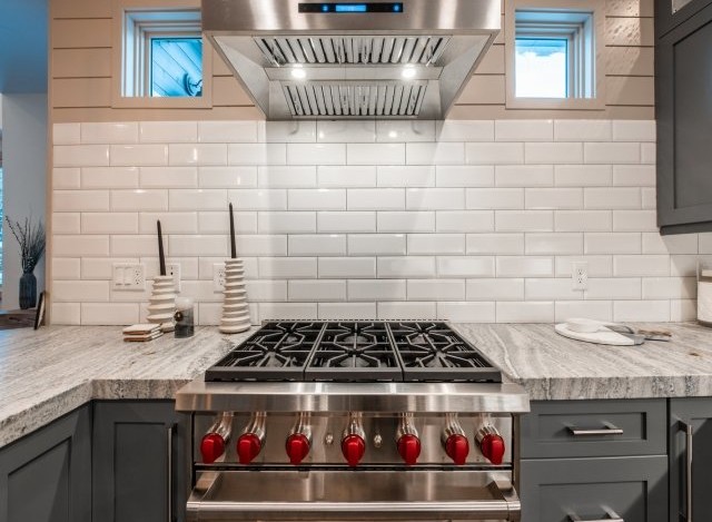 This stunning kitchen boasts a sleek, stainless steel range with red knobs, complemented by a white subway tile backsplash.