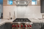 This stunning kitchen boasts a sleek, stainless steel range with red knobs, complemented by a white subway tile backsplash.