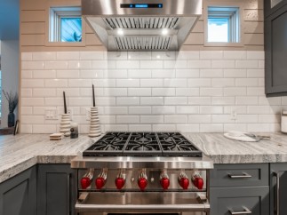 This stunning kitchen boasts a sleek, stainless steel range with red knobs, complemented by a white subway tile backsplash.