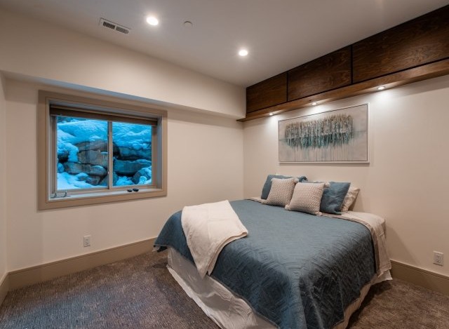 This stunning bedroom boasts a cozy and elegant design, featuring a plush bed with a soft, textured comforter and a large window offering breathtaking views of a snow-covered landscape.