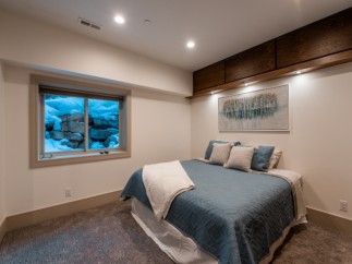 This stunning bedroom boasts a cozy and elegant design, featuring a plush bed with a soft, textured comforter and a large window offering breathtaking views of a snow-covered landscape.