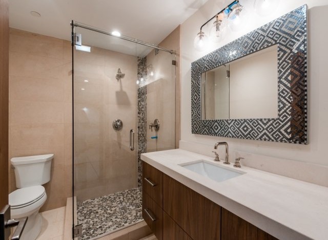 This stunning bathroom boasts a spacious shower with pebble flooring and glass enclosure, complemented by a sleek, modern vanity with a white countertop.