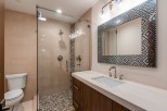 This stunning bathroom boasts a spacious shower with pebble flooring and glass enclosure, complemented by a sleek, modern vanity with a white countertop.