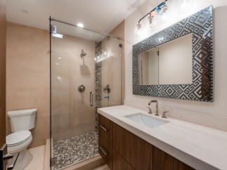 This stunning bathroom boasts a spacious shower with pebble flooring and glass enclosure, complemented by a sleek, modern vanity with a white countertop.