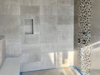 This stunning bathroom boasts a spacious shower with a built-in seat and a modern hexagonal mosaic tile accent wall.